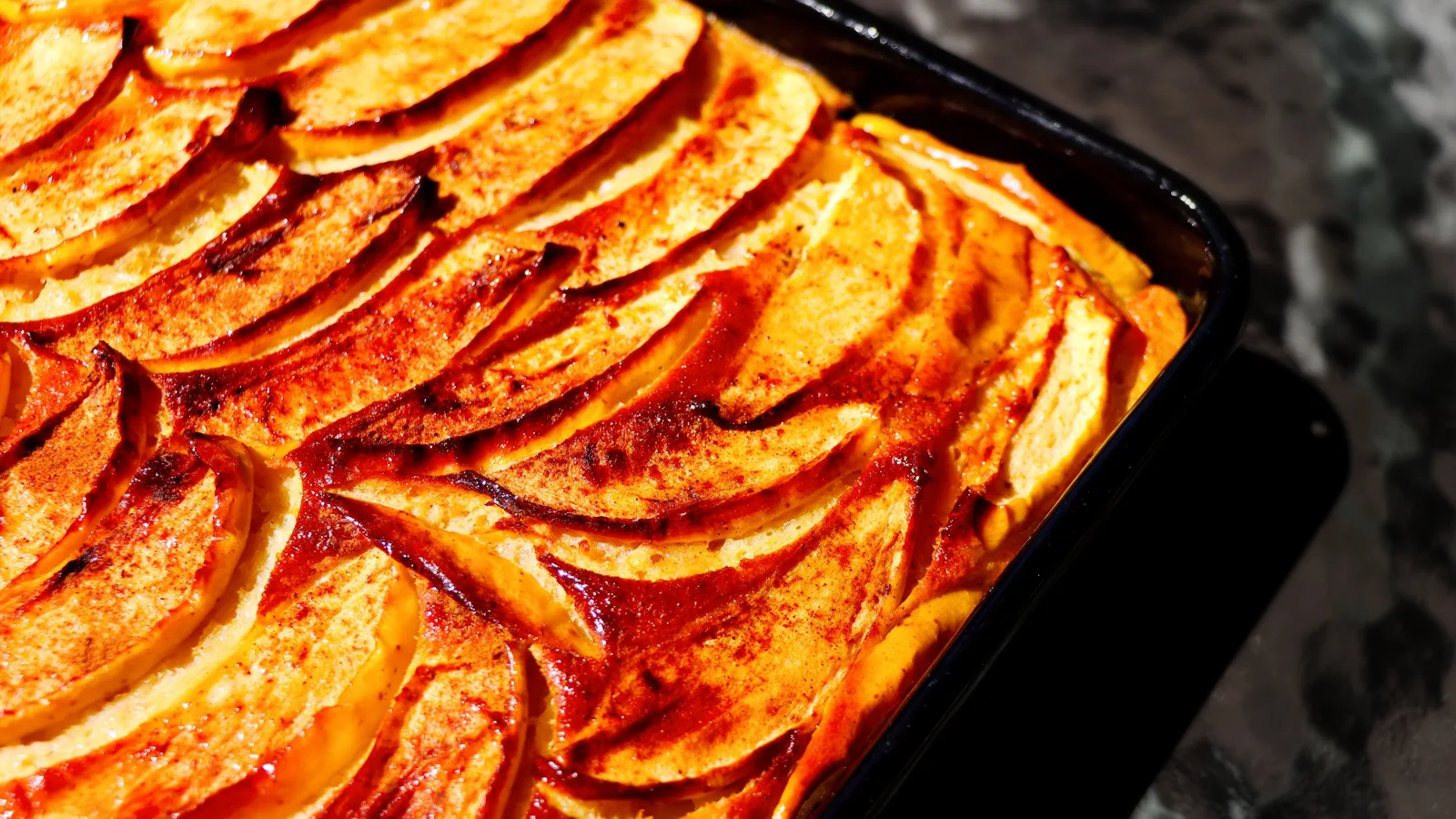 Clafoutis aux pommes doré dans un moule, tranches de pommes fondantes et surface saupoudrée de sucre glace.